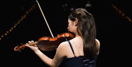 Skrzypaczka w ciemnych włosach stojąca tyłem do zdjęcia grająca na skrzypcach