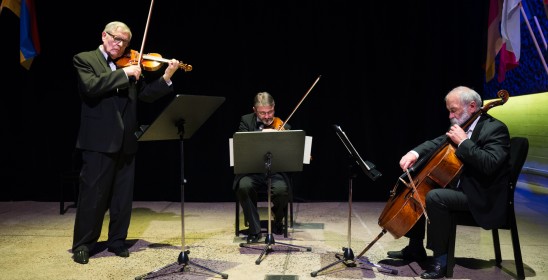 Trzech mężczyzn gra w trio skrzypcowym na scenie w sali kameralnej