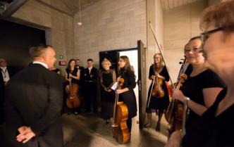 smiling musicians, women and men, listening to the conductor standing backwards