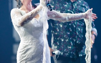 kobieta w białej sukni i mężczyzna we wzorzystej koszuli śpiewający do mikrofonu